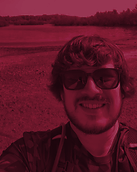 a heavily tinted photo of a man smiling at the camera. He has thick wavy hair and a beard and is wearing sunglasses
